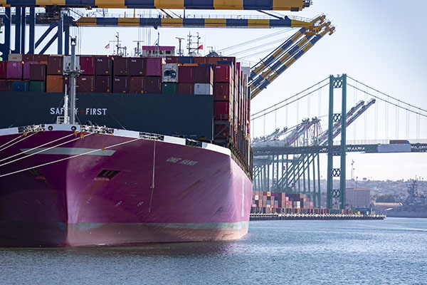 A pink container ship docked at YTI Terminal at the Port of Los Angeles with the bridge in the background