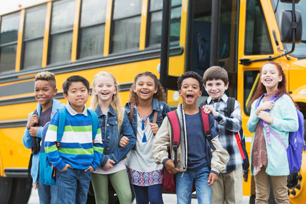 Children standing in front of yellow school bus.